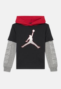 Haut à capuche noir à manches longues avec capuche rouge, présentant un logo Jordan blanc sur le devant et des manches grises avec "JORDAN" imprimé en blanc.