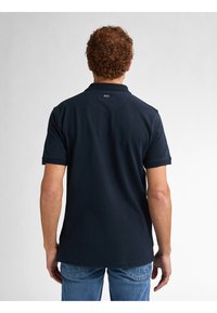 Marineblauw poloshirt met een klassieke kraag, korte mouwen en een rechte zoom. Gemaakt van een soepele, lichte stof met subtiele branding op de achterkant.