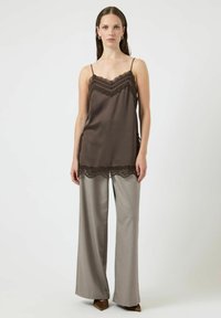 Brązowa satynowa koszulka na cienkich ramiączkach z koronkową lamówką, zestawiona z jasnoszarymi spodniami o szerokich nogawkach i butami na obcasie z szpiczastym noskiem.