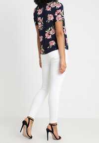 Navy short-sleeve top with pink floral pattern, paired with white skinny jeans and black high-heeled sandals. Smooth, lightweight fabric.