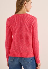 Pull en tricot rose vif avec des manches longues, texture côtelée, encolure ronde et ourlet ajusté, associé à un jean bleu.
