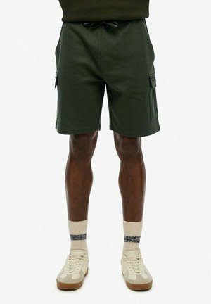 Cargo shorts i mørkegrøn stof med elastisk talje, snor og sidelommer. Båret med lyse sneakers og sokker.