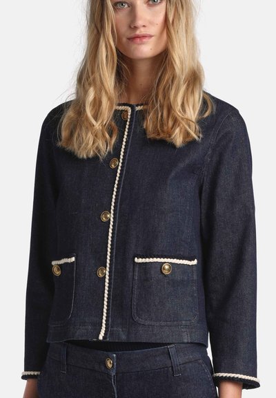 Mørk denimjakke med guldknapper, kontrasterende hvid kant langs kanter og lommer, med cropped design og to forlommer.