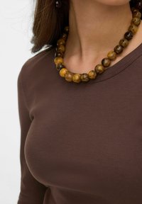 Sieraad met ronde parels die lijken op barnsteen, in tinten geel en bruin, gedragen over een bruin geribd topje.