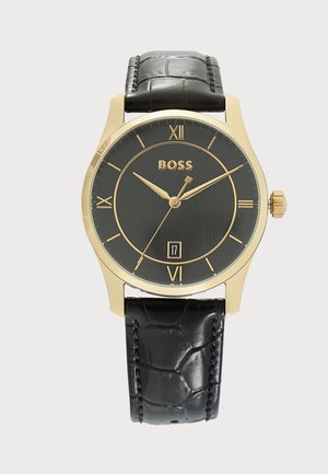 Guld-etui armbåndsur med sort urskive, romertal, datovisning kl. 6 og sort tekstureret læderrem.