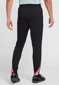 Pantalones deportivos negros con cintura elástica y detalles en rosa en el dobladillo. Tejido texturizado, ajuste slim, combinados con zapatillas deportivas negras.