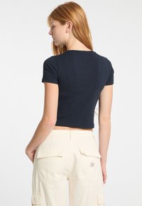 Jūros pajėgų stiliaus trumpa T-shirt su trumpomis rankovėmis, pagaminta iš minkštos medžiagos. Dėvima su šviesiai rudos spalvos kargo kelnėmis, turinčiomis kišenes su uždengimu. Švarus, paprastas dizainas.