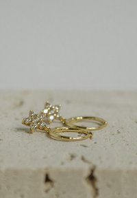 Pendientes de aro de oro con un diseño floral, adornados con múltiples gemas transparentes. Textura suave con un acabado pulido.