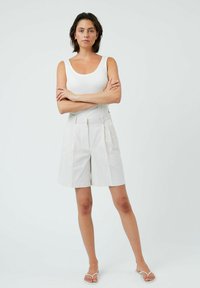Weißes, geripptes Tanktop kombiniert mit hellen, plissierten Shorts. Einfaches Design mit glatter Textur und minimalistischer Stilistik. Silberne Akzente auf den Shorts.