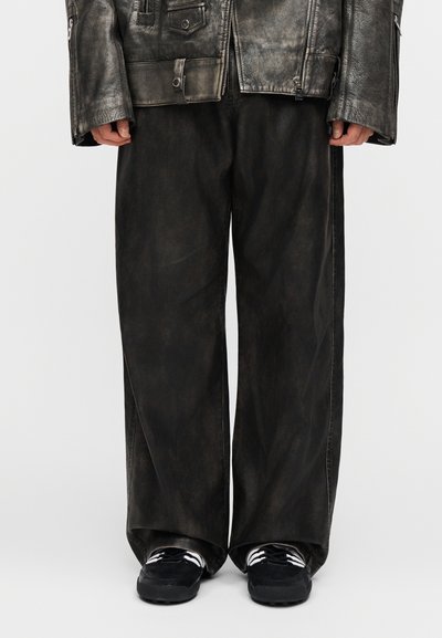 Mustad, laia lõikega püksid tuhmunud tekstuuriga. Sobitatud mustade tossudega, millel on valged triibud. Kandmiseks valitud kulunud nahast jakk.