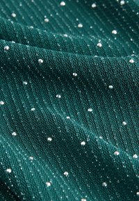 Emerald zelená textúrovaná tkanina s vertikálnym ryhovaním a roztrúsenými striebornými flitrami, vytvárajúca skvostný a elegantný vzhľad.