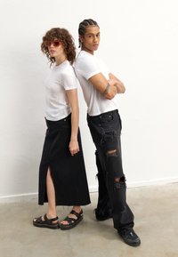 Jeans em denim preto com detalhes desgastados e uma t-shirt branca combinados com uma saia de denim preto com uma fenda lateral. Os acessórios incluem óculos de sol e sandálias.
