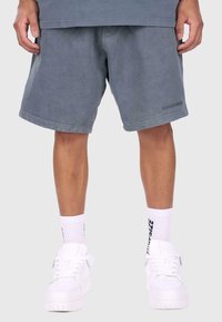 Grå bomuldsshorts med en afslappet pasform, der har et logo-detalje på kanten, kombineret med hvide høj-top sneakers og hvide ankelstrømper.