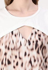 Tielko s krátkym rukávom s bielym živôtikom a výstrihom do V; dolná časť má leopardí vzor v béžových a hnedých odtieňoch.