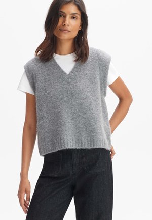 Grauer ärmelloser Pullover mit V-Ausschnitt, aus weichem, strukturiertem Strickmaterial, über einem weißen T-Shirt getragen, kombiniert mit dunklen Hosen.