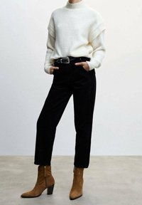 Pull en maille crème avec accents côtelés, pantalon en velours côtelé noir et bottines en daim beige à talon carré. Ceinture noire avec boucle argentée.