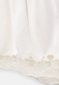 Gros plan d'un tissu blanc avec une bordure en dentelle florale festonnée le long du bord inférieur, montrant une texture fine et un motif délicat.
