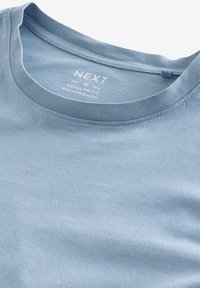 Svetlo modra bombažna majica s krojaškim ovratnikom, z gladko teksturo in natisnjenim oznakom, ki pravi "NEXT M REGULAR FIT, MADE IN BANGLADESH."