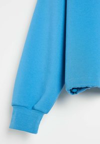 Jasnoniebieski rękaw bluzy z ribaną mankietu i detalem z guzikami, wykonany z teksturowanej tkaniny, prezentujący luźny krój.