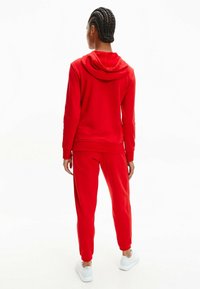 Hoodie en polaire rouge avec une capuche à cordon, associé à un jogging assorti. Doté de poignets et d'un ourlet élastiques, présenté de dos.
