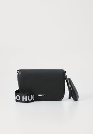 Black leather crossbody bag with flap and detachable zip pouch, featuring a wide black strap with white "HUGO" text.