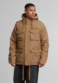 Parka multibolsillo en tono marrón, con capucha, cierre frontal de cremallera, cordón ajustable y tejido texturizado. Cuenta con cierres de botón y detalles de bolsillos de parche.