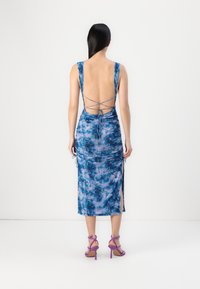 Robe mi-longue à fleurs bleues avec un dos nu et des détails lacés, dotée de fentes sur les côtés et d'une texture froncée. Associée à des sandales à talons hauts violettes.