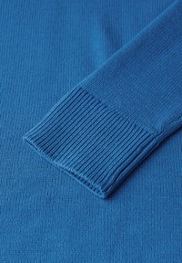 Détail d'un pull en tricot bleu montrant la texture côtelée des poignets, un tissu lisse et une couleur uniforme. Design léger et flexible.