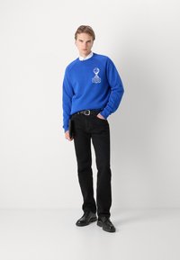 Blauwe sweatshirt met logodetail, gecombineerd met zwarte jeans en zwarte schoenen. Gladde stof, relaxte pasvorm, ronde halsontwerp en lange mouwen.