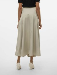 Beige, flat maxi kjol med en mjuk textur, med hög midja och utsvängd design, kombinerad med ljusa, spetsiga klackskor.