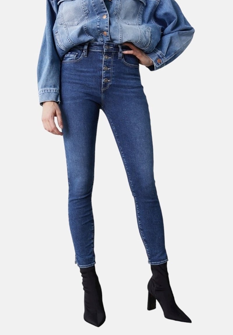 Hoge taille blauwe denim jeans met een vijfknops voorkant, aansluitende pasvorm en minimale beschadiging, gecombineerd met zwarte stiletto enkellaarsjes.