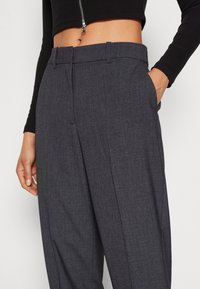 Mörkgrå skräddarsydda byxor med en mjuk textur, framfickor och en slät framsida. Har en standard midja för en klassisk passform.