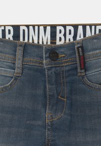 Tmavě modré džíny z denimu s kontrastním oranžovým švem, s knoflíkovým zapínáním, předními kapsami a elastickým pasem s logem.