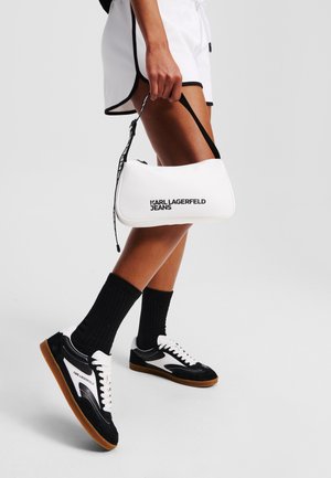 Bolso blanco con forma curva, logotipo negro "KARL LAGERFELD JEANS," combinado con zapatillas deportivas en blanco y negro y calcetas negras hasta la rodilla.