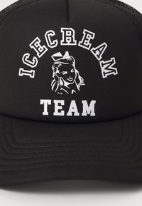 Svart caps med flat skygge og mesh bak. Inkluderer hvit tekst "ICECREAM" som buer over en grafikk av en kvinne, med "TEAM" under.