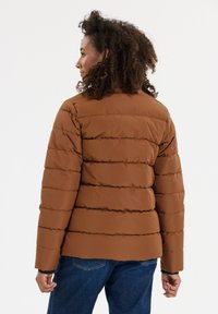 Brun pufferjakke med quiltet design, lange ærmer og en let cropped pasform. Materialet fremstår glat med en mat finish.