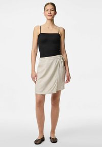 Czarny top na ramiączkach z cienkimi paskami w połączeniu z jasnobeżową spódnicą kopertową z zapięciem na węzeł, gładką fakturą i długością do kolan.