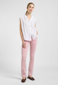 Camisa blanca de manga corta con botones y un patrón texturizado, combinada con unos jeans ajustados de color rosa claro y zapatos de tela trenzada de color marrón.