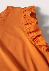 Haut en coton orange avec un bord volanté texturé orné de détails en broderie anglaise le long de l'encolure, tissu lisse et coupe décontractée.