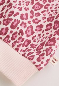 Rosa och mörkröd leopardmönstrad tyg med en ljusrosa ribbad mudd och en liten etikett med texten "happy days"