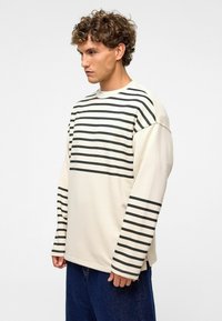 Crème shirt met lange mouwen, voorzien van horizontale zwarte strepen op de borst en mouwen, met een relaxte pasvorm en geribde manchetten.