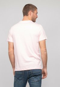 T-shirt à manches courtes rose clair en tissu doux, avec un col rond classique et une coupe décontractée, porté avec un jean en denim bleu.