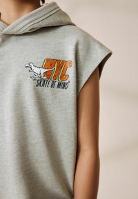 Haut sans manches gris en tissu doux présentant un graphique coloré "NYC Skate of Mind" avec un dinosaure sur une planche à roulettes.