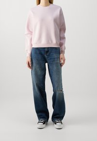 Ljust rosa bomullströja med rund hals, ribbade muddar och nederkant; kombinerad med löst sittande, bleka blå jeans med hål.