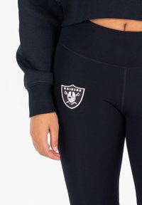 Zwarte leggings met een strakke pasvorm, voorzien van een wit Raiders-logo op de bovenbeen en gemaakt van een gladde, rekbare stof voor comfort.