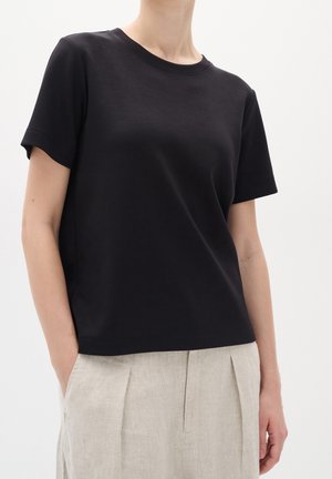 Schwarzes Baumwoll-T-Shirt mit kurzen Ärmeln und Rundhalsausschnitt, kombiniert mit hellbeigen Leinenhosen mit Falten. Glatte Textur.