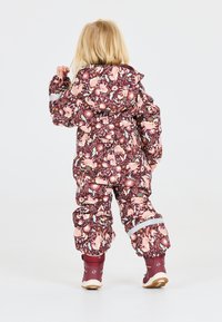 Kleurrijke paarse sneeuwpak met bloem- en dierenpatronen; voorzien van een capuchon, elastische manchet en reflecterende accenten; gecombineerd met bruine laarzen.