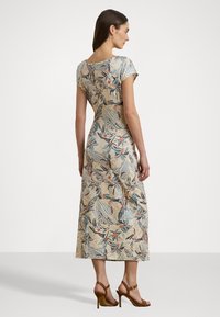 Vestido de tecido leve com padrão floral, até aos joelhos, com mangas curtas e costas em forma de scoop. Com sandálias de salto alto castanhas.