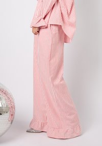 Rosa og hvitstripete, vid bukse laget av lett stoff, med utsvingt kant og diskret volangdetalj nederst.