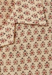 Blommig bomullstyg i crème med små, spridda bordeaux- och gröna blommor. Mjuk textur med ett subtilt ribbat mönster.